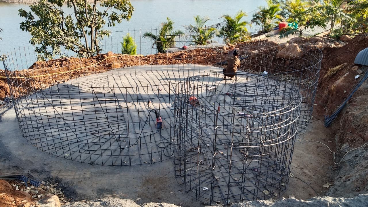 Circular reinforcement cages tied out on a poured slab beside the lake during construction of the pools at Aandra Lakestay Resort