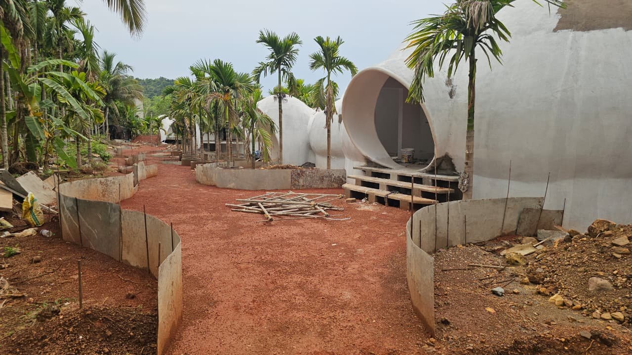 A row of ferrocement dome shells along a laterite path, one with a large circular tunnel entrance, during construction