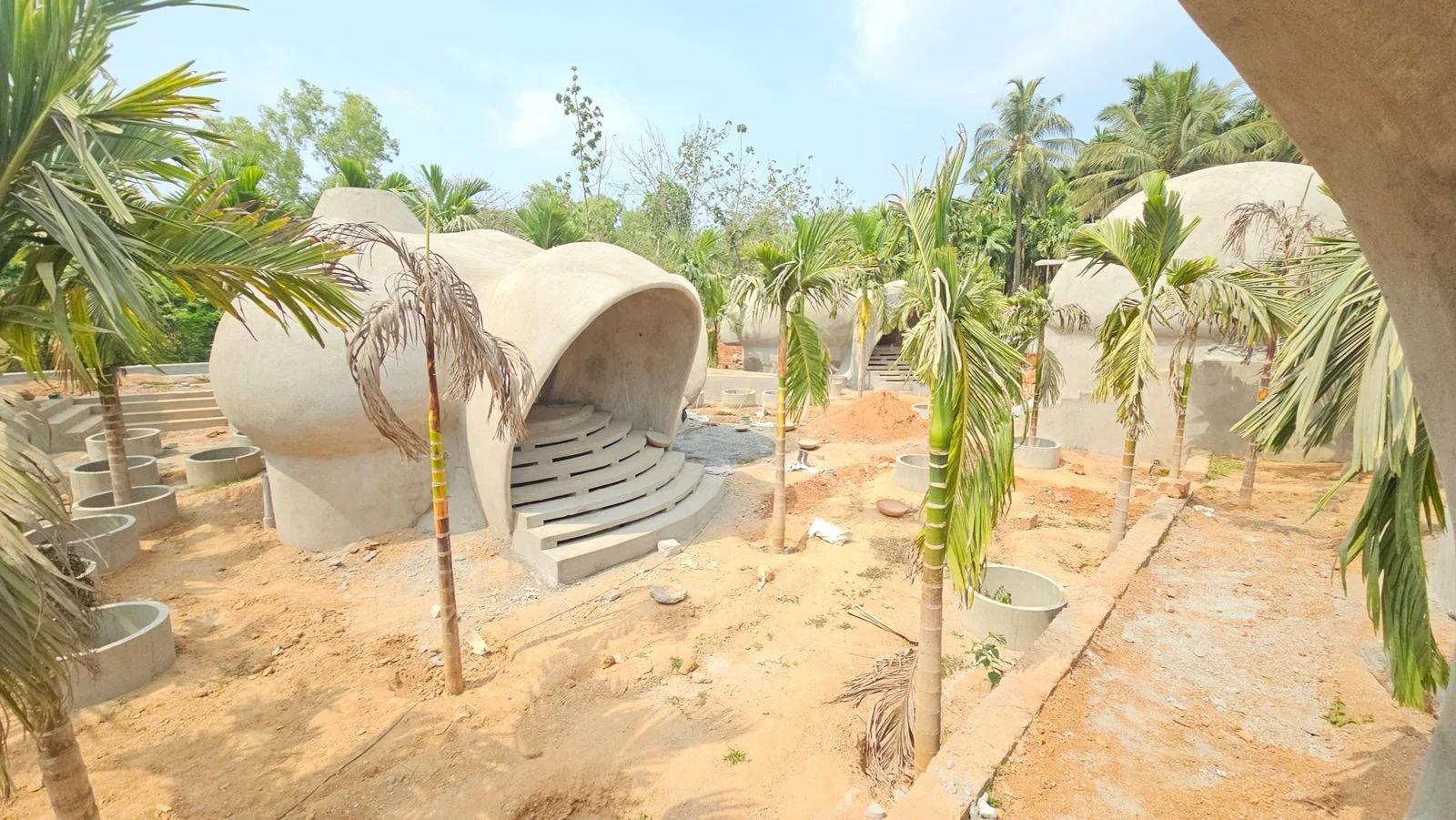 Dome cluster at AKAYA Resort, Gokarna mid-construction — mortar shells, newly planted palms, drainage rings and laterite paths being laid