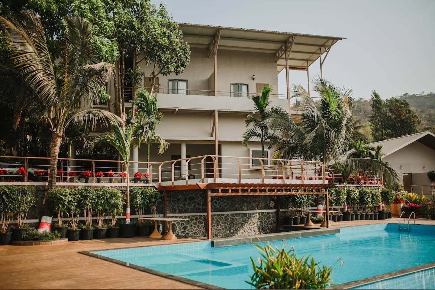 The three-storey guest block with stone-clad base and pergola, seen from the pool deck