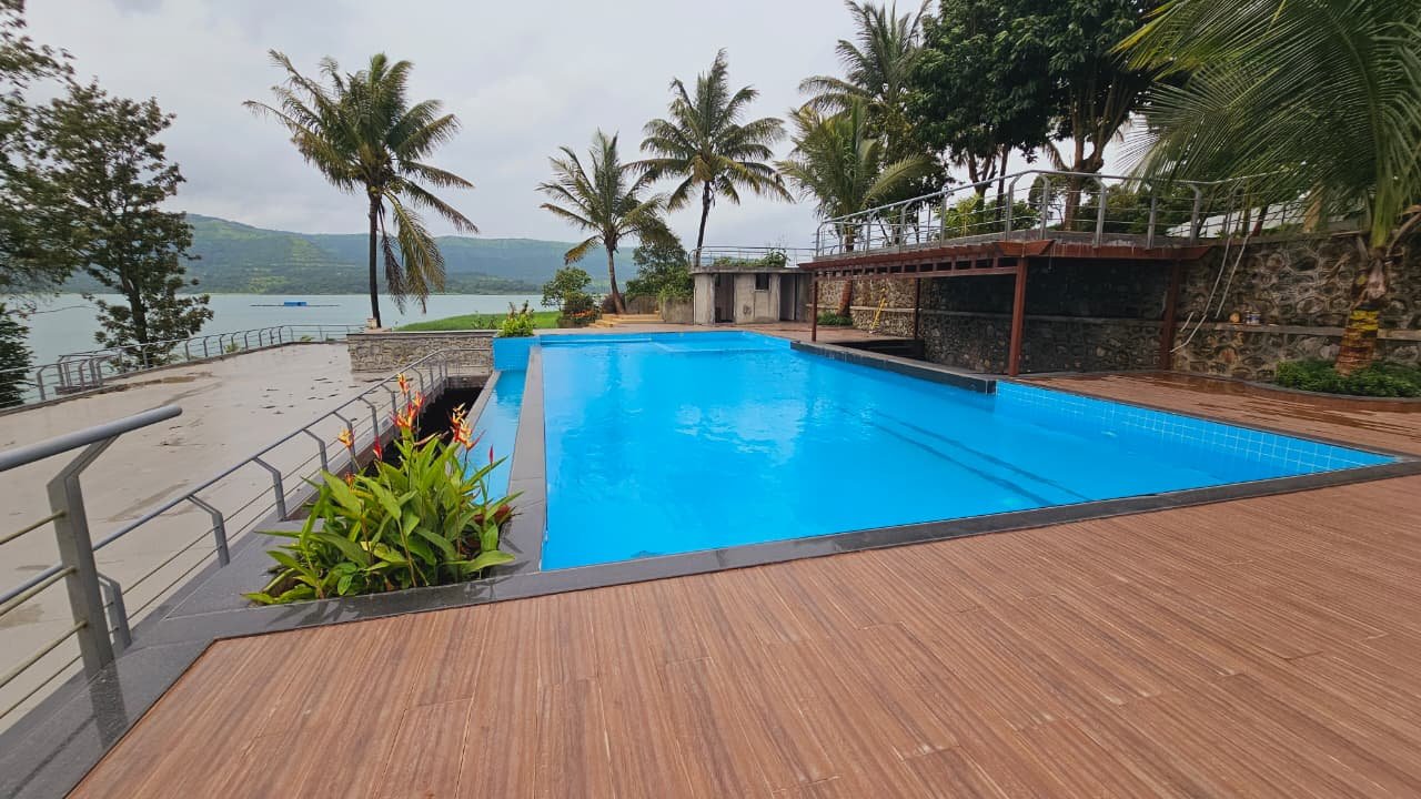 The infinity-edge pool and timber deck against green monsoon hills and the reservoir