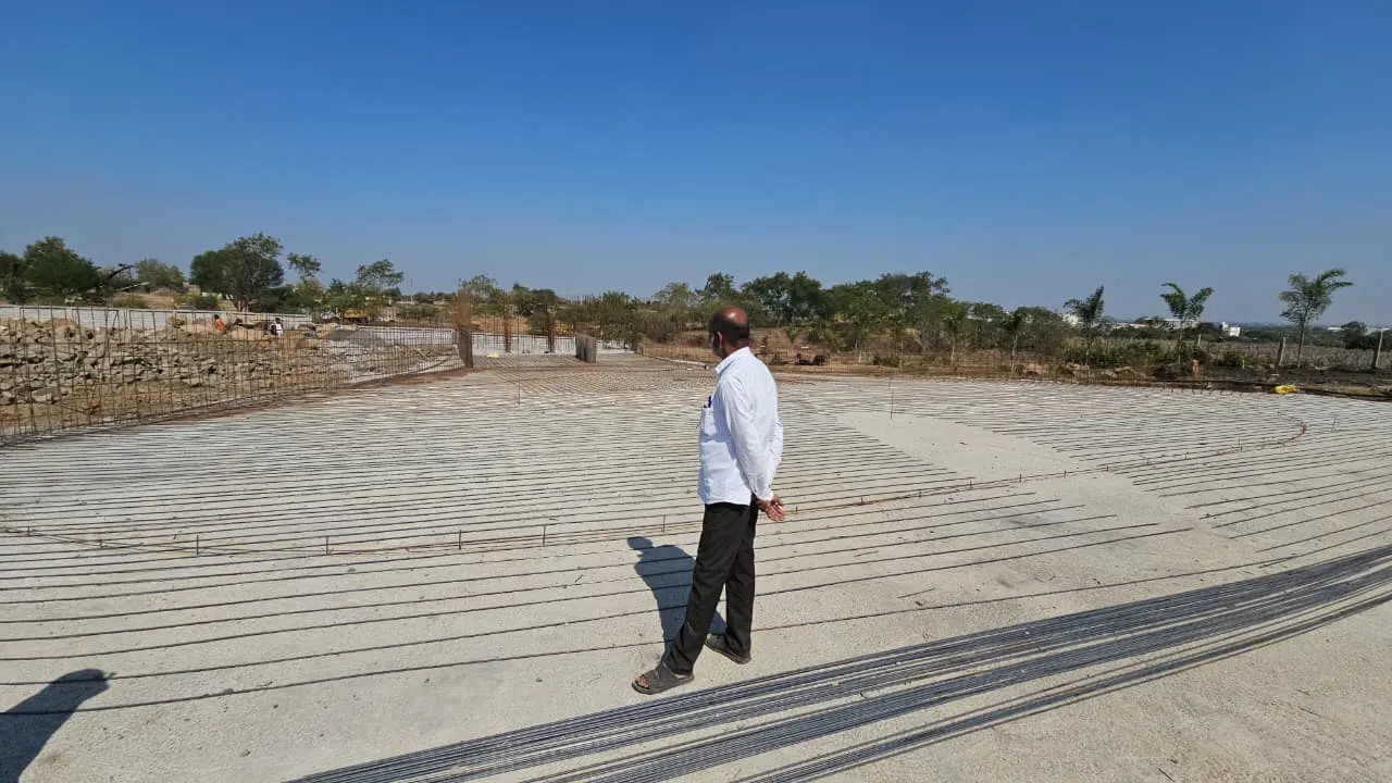The Aero City Water Park site under construction — a large free-form pool footprint laid out in reinforcement steel, with a PBJ Infra engineer walking across it
