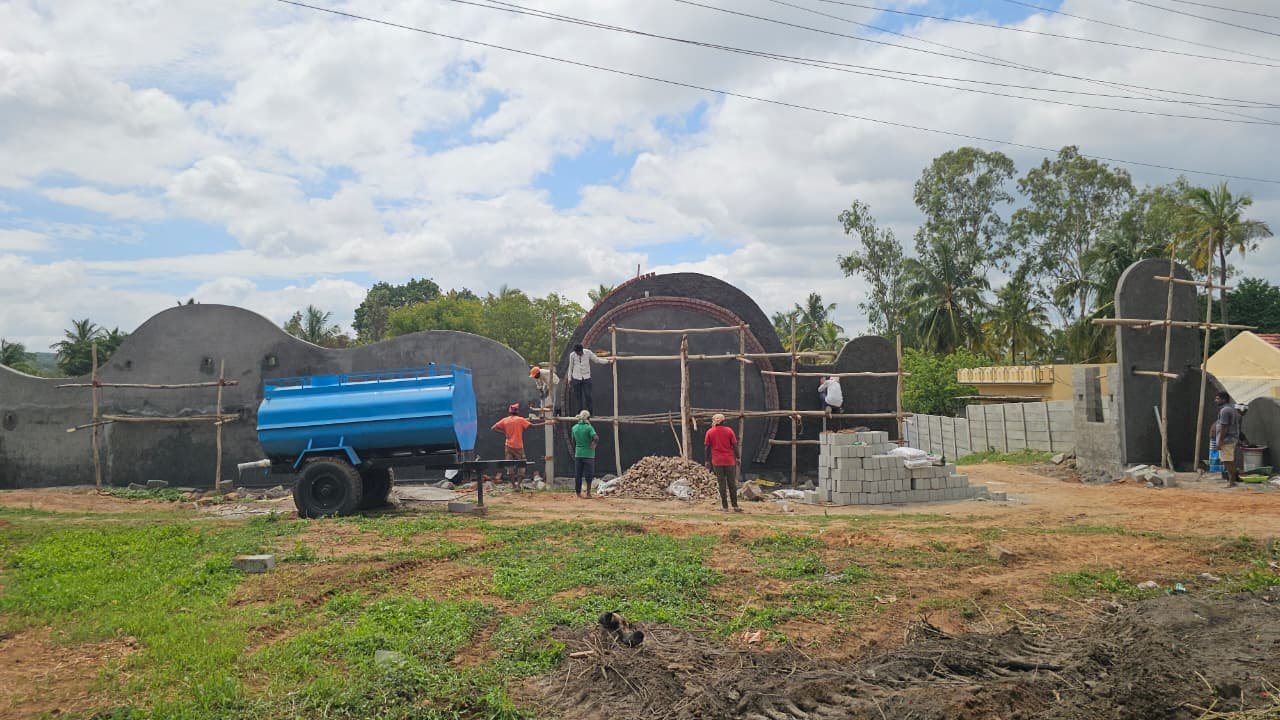 The Mi Casa wall under construction — grey plaster over blockwork, the brick-ringed portal, scaffolding and a water bowser on site