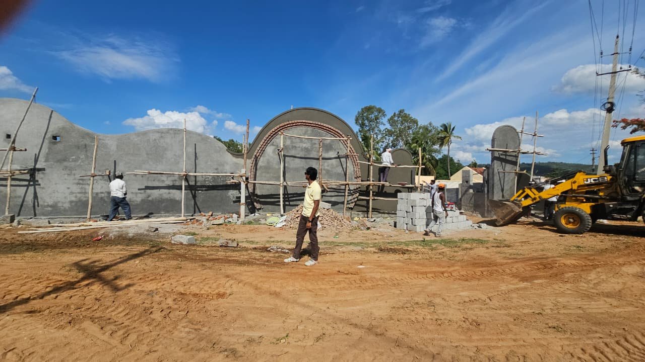 The Mi Casa entrance wall from an angle during construction, with a backhoe loader and material stacks on the cleared site
