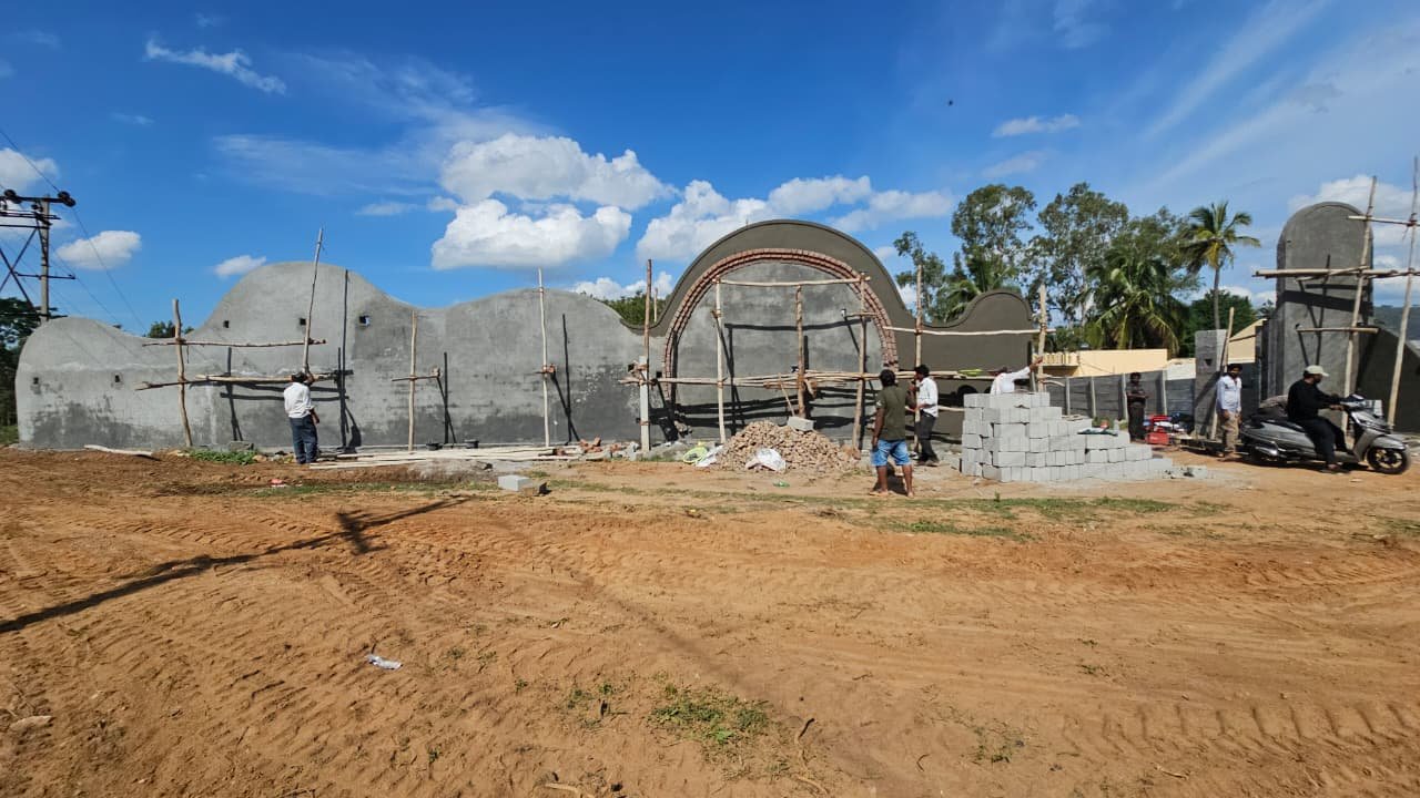The free-form Mi Casa boundary wall seen head-on during construction, its curved profile and circular opening in grey render