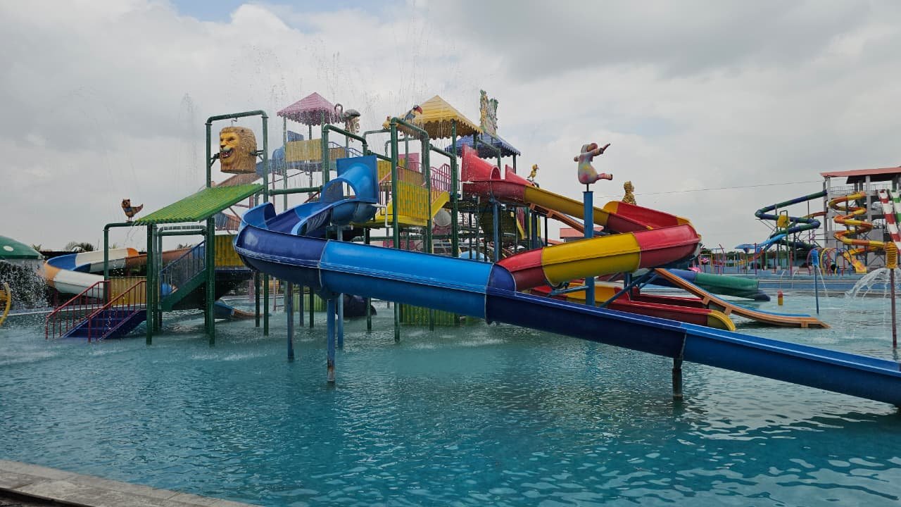 Blue tube slide curving out of the main play structure into the activity pool, with a lion-head fountain alongside